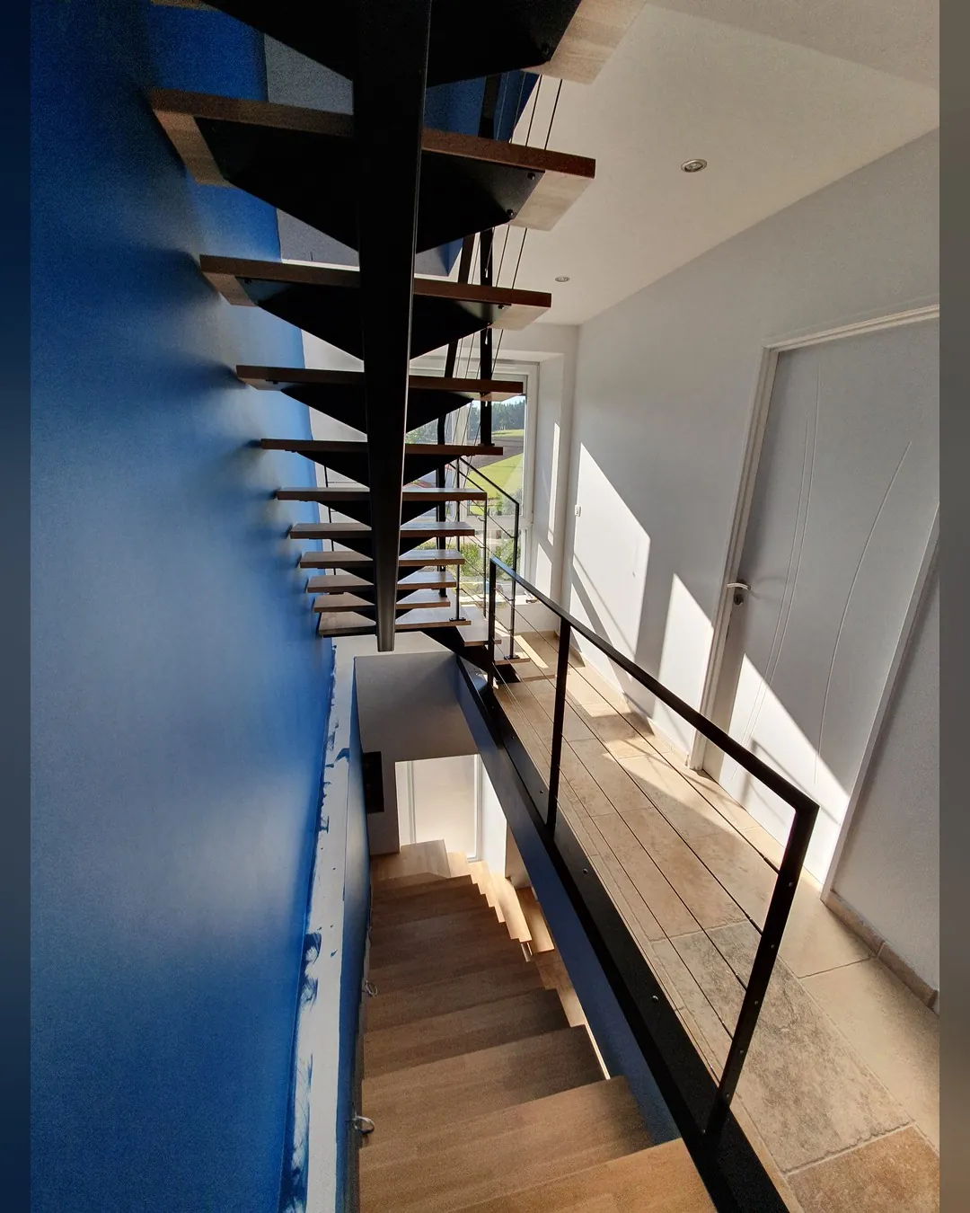 Escalier suspendu à limon central, marches bois, mur bleu
